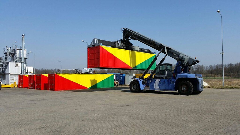 A crane lifts a container painted in red, yellow, and green, next to four identical containers.